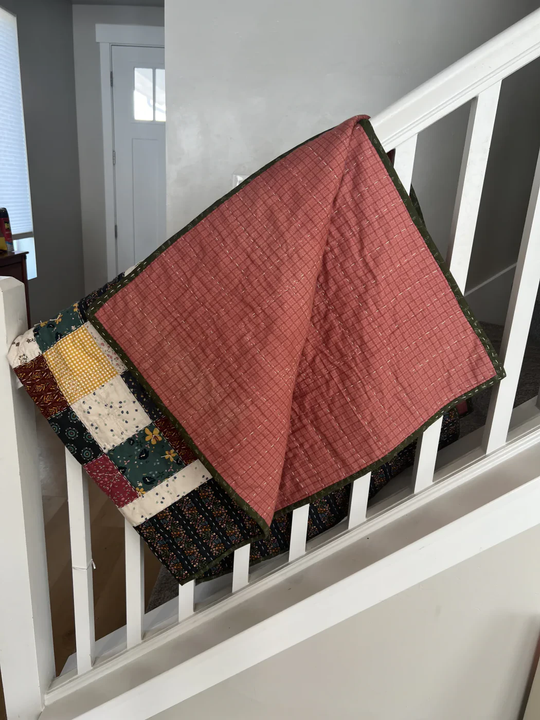 Pink quilt backing with rows of hand stitching and a dark green binding along the edge